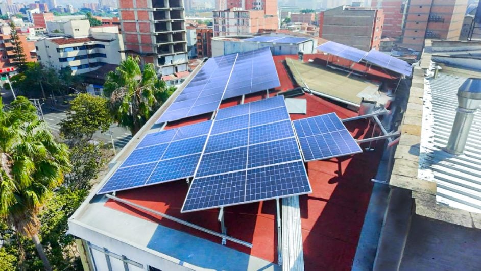 Paneles solares sobre una cubierta roja en medio de edificios.