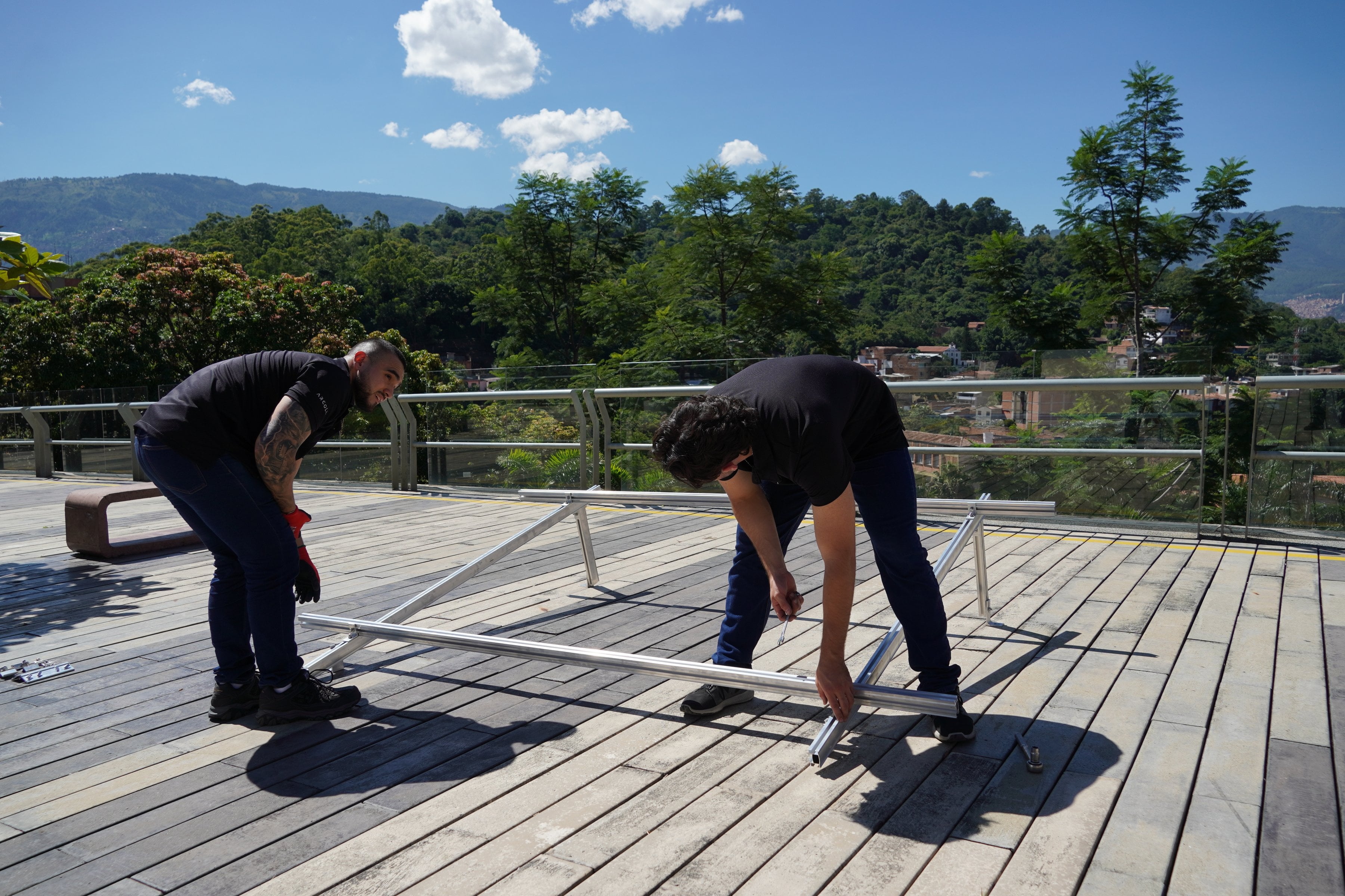 Dos instaladores armando una estructura de aluminio Arcoli para paneles solares en una terraza, con montañas al fondo.