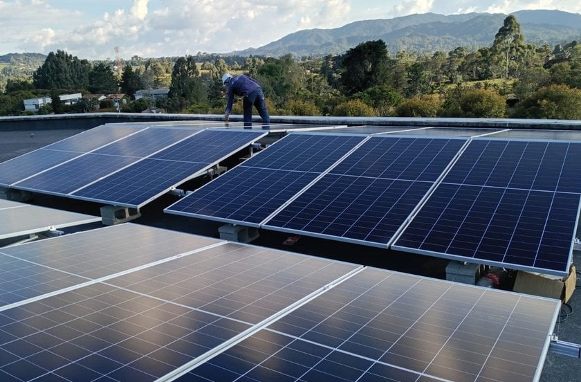 Instalador revisando filas de paneles solares sobre estructuras de aluminio en una losa, con montañas al fondo.