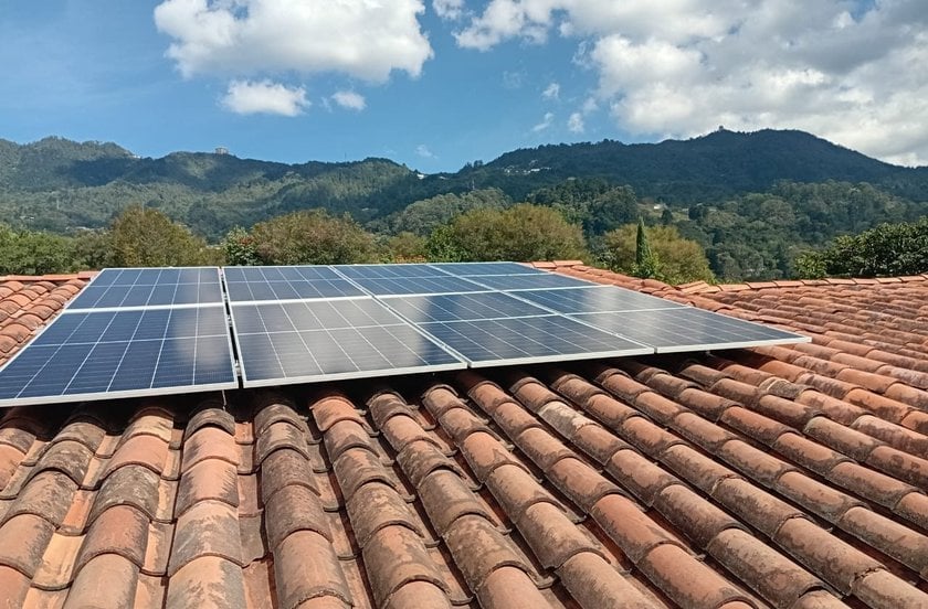 Paneles solares sobre estructura de aluminio en un techo de teja de barro, con montañas al fondo.