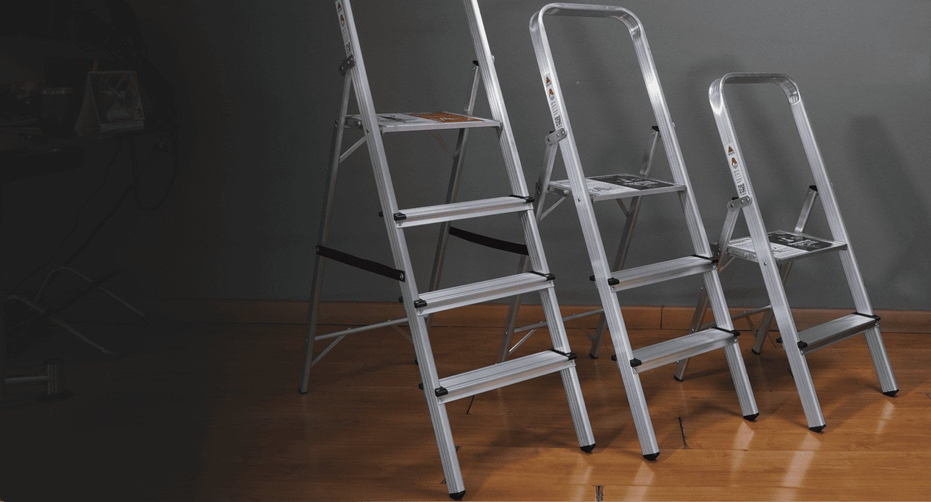 Las tres escaleras de aluminio Arcoli, de 3, 2 y 1 peldaños, sobre un piso de madera.